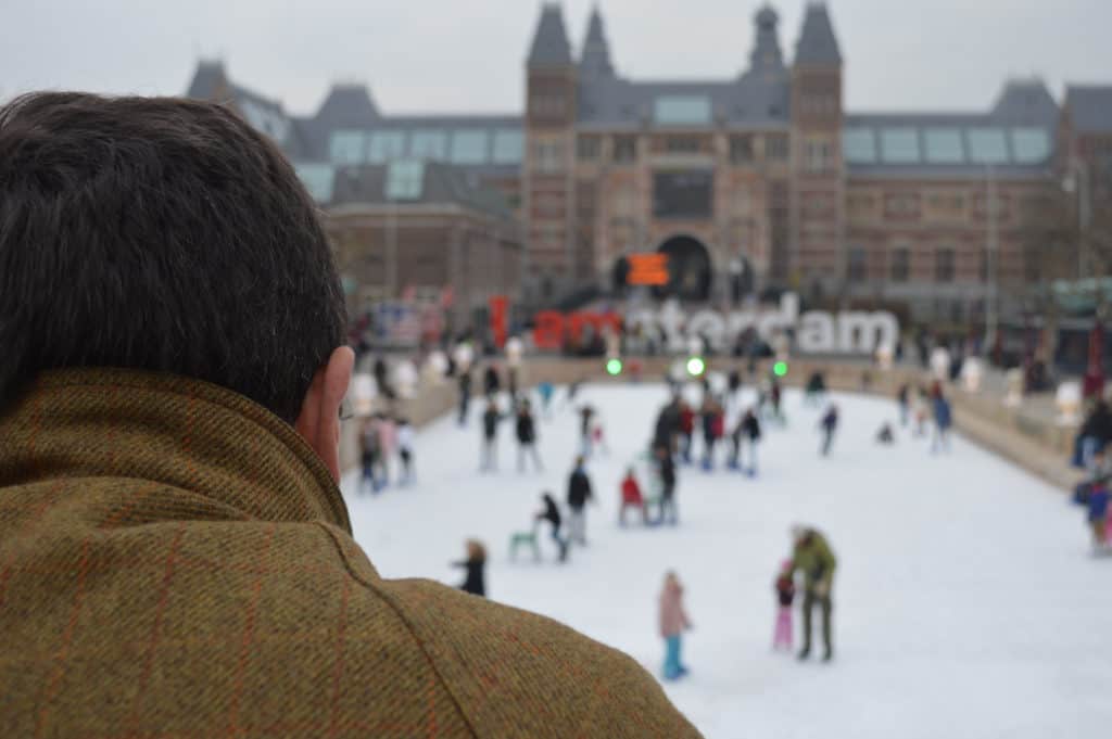 Man kijkt naar schaatsers Museumplein Amsterdam Man kijkt naar schaatsers op het Museumplein in Amsterdam